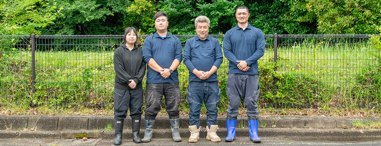 従業員が草むらの前で横に並んで写っている様子